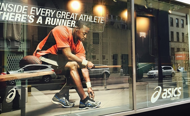 Storefront window graphic featuring a running athlete, promoting an athletic brand with bold text.